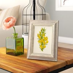 two vases with flowers are sitting on a table next to a framed painting and lamp