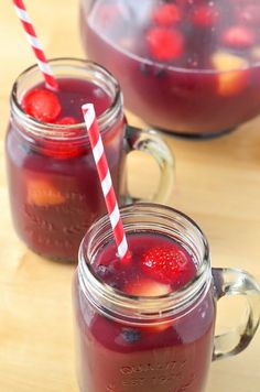 two mason jars filled with raspberry punch and topped with strawberries, sitting on a table