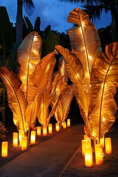 lighted candles are lined up along a path with palm leaves in the foreground and onlookers behind them