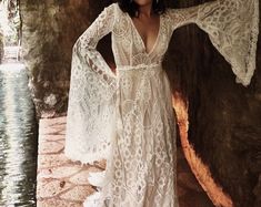 a woman standing in front of a tree wearing a white lace dress with long sleeves