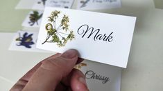 a person holding up a business card with flowers on it and the words mark written in black ink