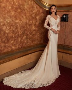 a woman standing in front of a wall wearing a wedding dress with long sleeves and an open back