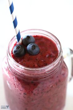 a jar filled with blueberries and smoothie on top of a white table next to a straw