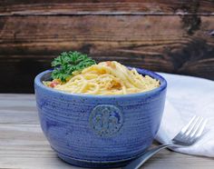 a blue bowl filled with pasta and garnished with parsley next to a fork