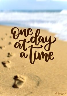 the words one day at a time written in brown ink on a sandy beach with footprints