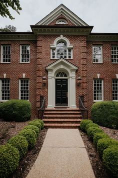 an old brick house with steps leading to the front door and two large bushes on either side