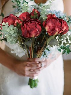 a woman holding a bouquet of red flowers in her hands and wearing a white dress