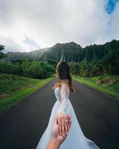 a bride and groom holding hands while walking down the road