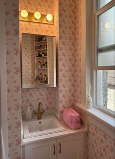 a bathroom sink sitting under a mirror next to a window with pink flowers on it