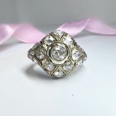 an antique diamond ring is shown on a white surface with a pink ribbon behind it