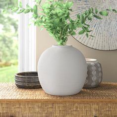 a white vase sitting on top of a wooden table next to a plant in it