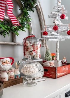 an assortment of candy and christmas decorations on a white table with a mirror in the background