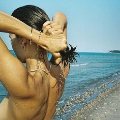 a woman standing on top of a beach next to the ocean holding her hair back