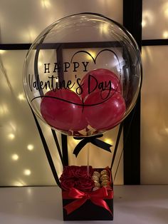 two heart shaped balloons in a clear box with red ribbon and bow around it, sitting on a table