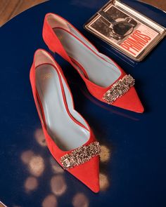 a pair of red shoes sitting on top of a blue table next to a book