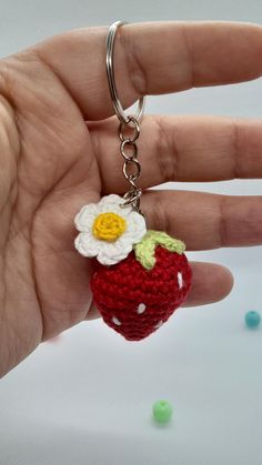 a hand holding a tiny crocheted strawberry keychain with a flower on it