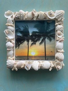 a photo frame with shells and palm trees in front of a sunset on the beach