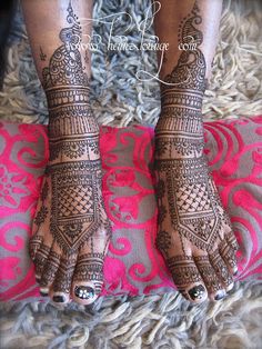 two feet with henna tattoos on them and one is standing on a pink blanket