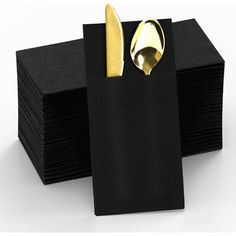 a stack of black napkins with gold spoon and fork sticking out of it's pocket