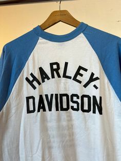 "1980s Harley Davidson blue and white baseball t-shirt. Unworn and Unwashed. Measurements flat: 19\" Pit to Pit 32\" Length All sales final, please ask any questions you have before purchasing! Thank you!" Casual Blue Baseball Jersey With Letter Print, Blue Cotton Baseball Jersey With Letter Print, White Throwback T-shirt For College, Retro Crew Neck T-shirt With Lettering, Vintage Short Sleeve T-shirt With Lettering, Sporty Blue Cotton Baseball Jersey, Blue Cotton Sporty Baseball Jersey, Blue Graphic Print Baseball Jersey For Baseball Season, Blue Baseball Jersey With Letter Print For Streetwear