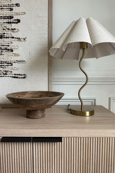 a table lamp sitting on top of a wooden cabinet next to a bowl with an umbrella shade