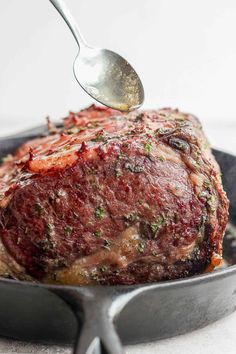 a piece of meat is being cooked in a skillet with a spoon and fork