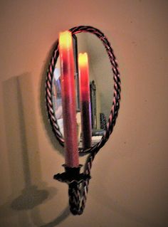 three candles are lit in front of a mirror with rope around the edges and hanging on a wall