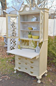 an old china cabinet painted yellow with white trim and gold accents, sits outside in the grass