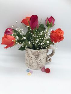 a mug filled with red roses and baby's breath next to candies on a white surface