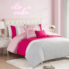 a bedroom with pink and grey bedding, white rugs and a neon sign on the wall