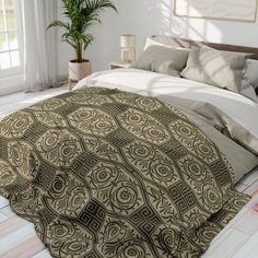 a large bed covered in a brown and white comforter next to a plant on top of a hard wood floor