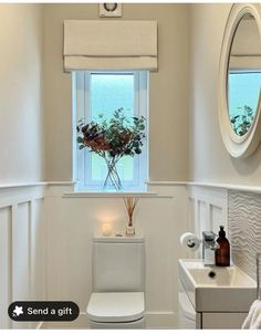 a white toilet sitting next to a sink in a bathroom under a window with a flower vase