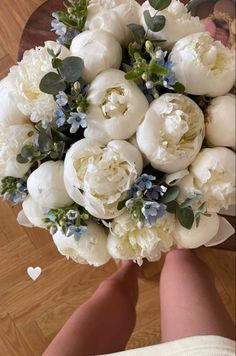 a bridal bouquet with white flowers and greenery in someone's hand on a wooden floor