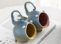 two blue ceramic fish shaped vases sitting on top of a book next to each other