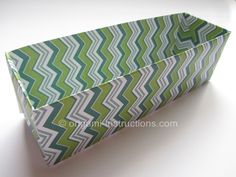 an origami box with green and white chevrons on the inside, sitting on a table