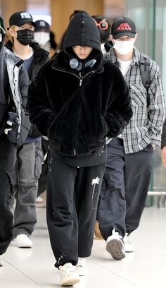 a group of people walking down a hallway wearing face masks and black coats on their faces