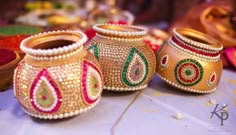 three decorated pots sitting on top of a table next to each other with gold trimmings