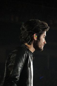 a man in black leather jacket and ear piercings looking off into the distance at night