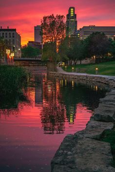 the sun is setting over a river with buildings in the background