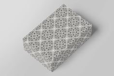 a gray and white patterned tie laying on top of a grey surface with an intricate design