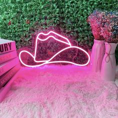 a pink neon sign sitting on top of a bed next to a vase filled with flowers