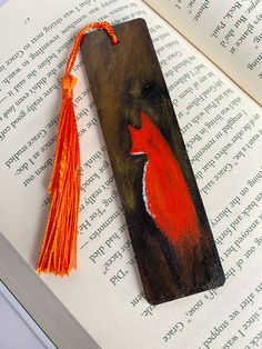 a bookmark with an orange fox painted on it and tassels attached to it