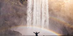 a man standing in front of a waterfall with his arms wide open under a rainbow