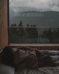 a person laying in bed with their head on the window sill looking out at mountains