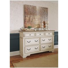 a white dresser sitting on top of a hard wood floor next to a painting above it