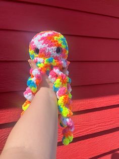 a hand holding an octopus stuffed animal with multi - colored yarns on it's arm