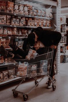 a man and woman sitting in a shopping cart at the grocery store with their feet on each other's head