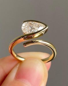 a hand holding a gold ring with a pear shaped diamond