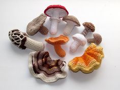 several crocheted mushrooms are arranged in a circle on a white surface, including one mushroom