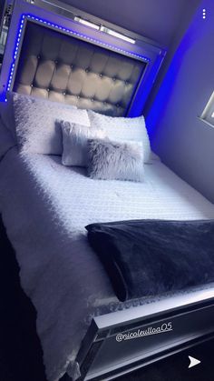 a bed with white sheets and pillows in a room that has blue lights on the walls